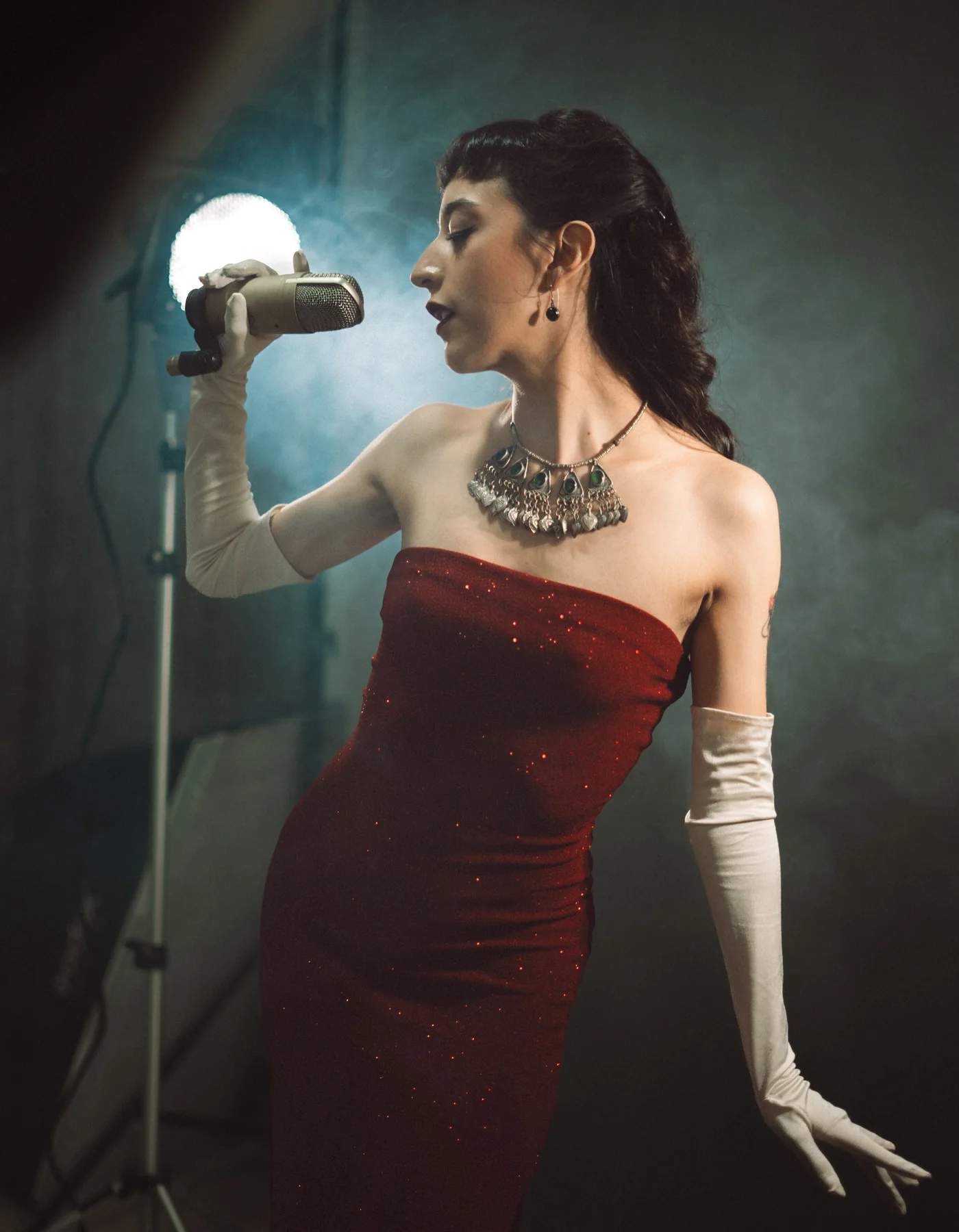 En performer i en palletbesat rød kjole, der synger i en mikrofon i vintage-stil under en spotlight